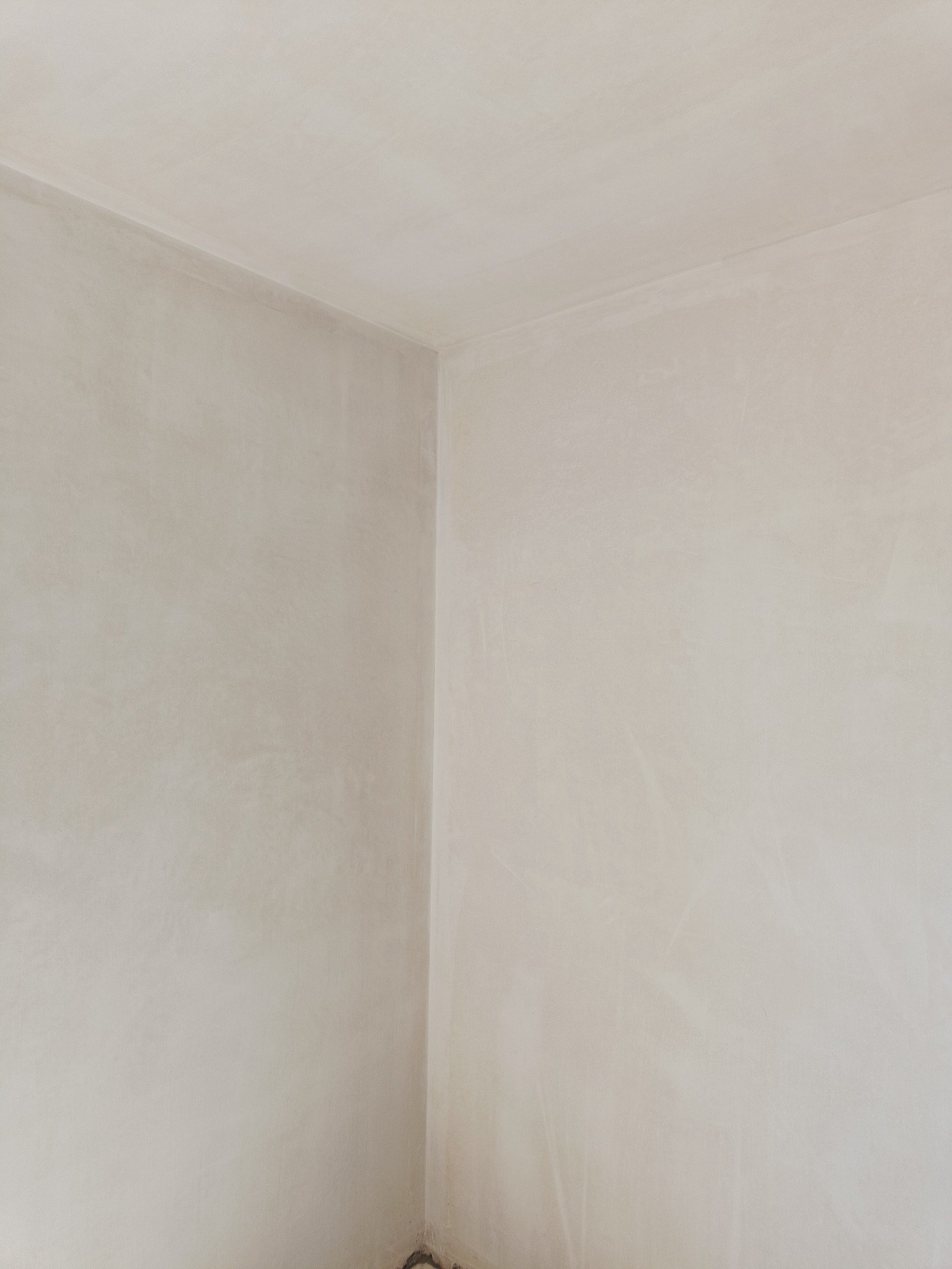 Świeżo położone, jasne tynki na ścianach i suficie w rogu pokoju, widoczne delikatne smugi i faktura powierzchni.