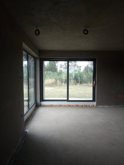 Wnętrze surowego domu po nałożeniu gładzi na ścianach i suficie, widoczne okna przesuwne z widokiem na zewnątrz.