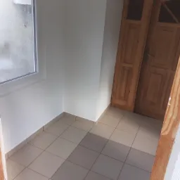 Wnętrze po remoncie: świeżo pomalowane ściany na biało, ułożona jasna terakota w szachownicę, widoczne drewniane futryny drzwi i okna.