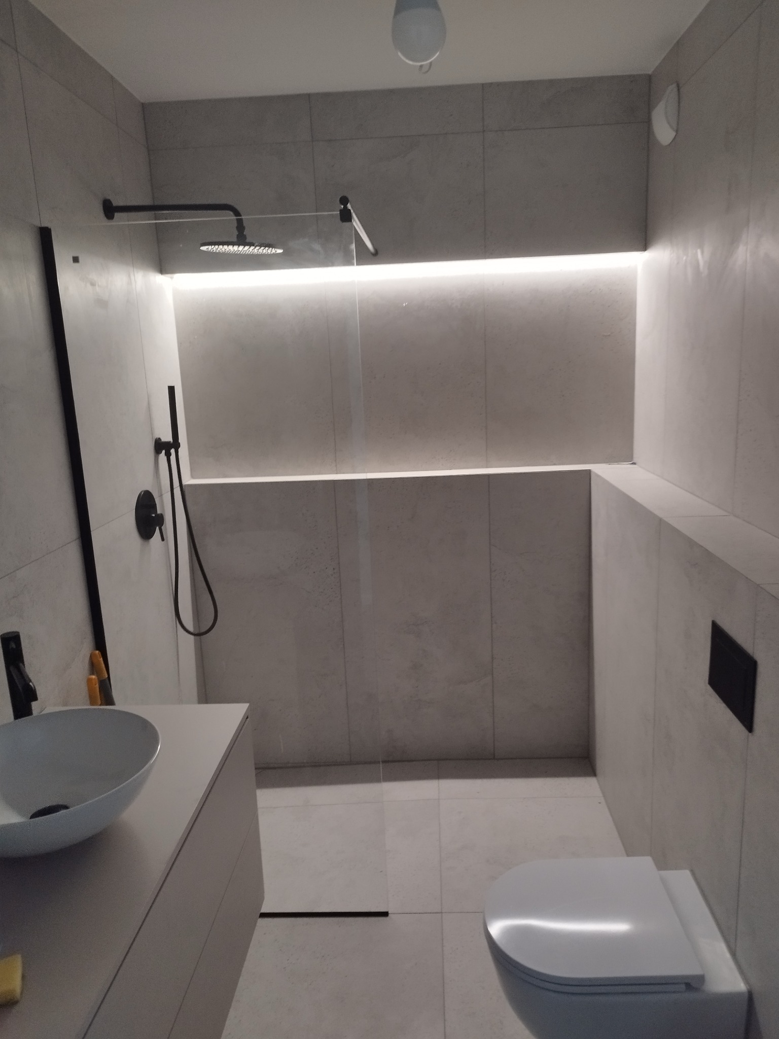 Nowoczesna łazienka z kabiną typu walk-in, szare płytki, podświetlenie LED, czarna armatura i umywalka nablatowa. Minimalistyczny design.