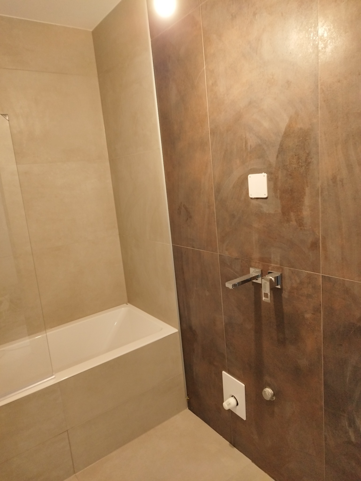 Wykończona łazienka: beżowe i brązowe płytki, minimalistyczna armatura, wanna z parawanem. Kontrast kolorów i faktur, nowoczesny design.