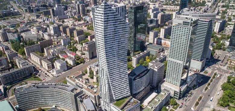 Panoramiczny widok z lotu ptaka na centrum Warszawy z nowoczesnymi wieżowcami i budynkami biurowymi w słoneczny dzień.