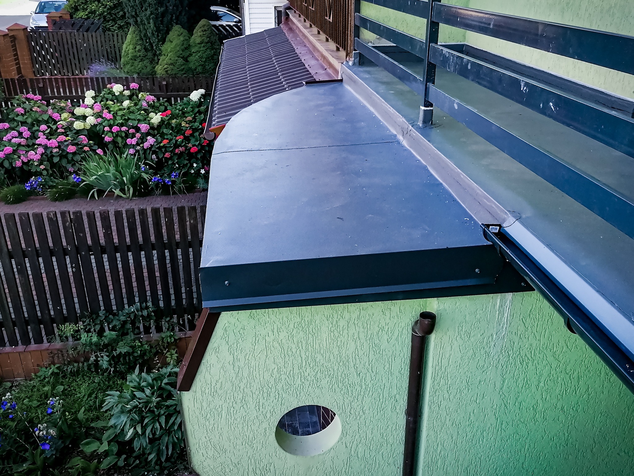 Wykończony dach z papy termozgrzewalnej w Miedzianej Górze, widok z góry na zieloną elewację domu z rynną i ozdobnym okrągłym otworem wentylacyjnym.