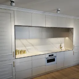 Nowoczesna kuchnia w odcieniach bieli z marmurowym blatem i złotymi akcentami, wbudowany piekarnik Bosch, trzy złote pojemniki na blacie.