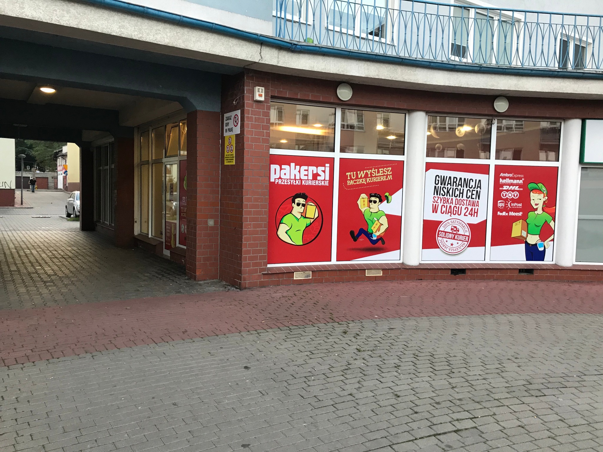 Lokal firmy kurierskiej Pakersi w Stargardzie, z reklamami na oknach przedstawiającymi kreskówkowe postacie niosące paczki i hasła o szybkich przesyłkach i niskich cenach.