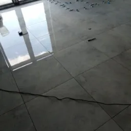 Układanie szarych płytek podłogowych z użyciem klips&oacute;w poziomujących w Mławie, widoczne odbicie okna w polerowanej powierzchni.