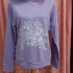 Liliowa bluza z kapturem, ozdobiona białym, abstrakcyjnym rysunkiem z podpisem 'Anna 23', prezentowana na manekinie z perłowym naszyjnikiem, na tle czerwono-białych pionowych pasów.