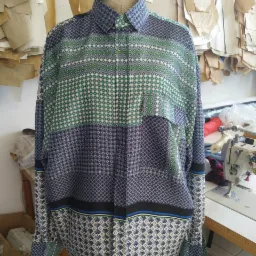 Wzorzysta koszula męska z długim rękawem na manekinie krawieckim, widoczna maszyna do szycia i wykroje papierowe w tle.