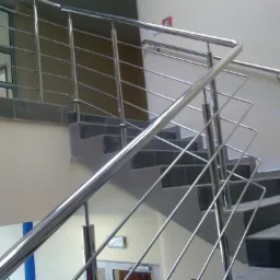 Wewnętrzne schody z szarymi płytkami i metalową, minimalistyczną balustradą ze stali nierdzewnej z poziomymi prętami, widok z dołu.