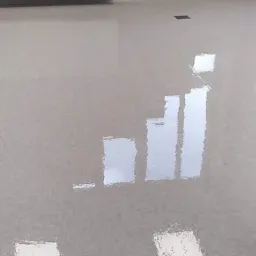 Świeżo wylana, błyszcząca posadzka w jasnoszarym odcieniu, z widocznymi refleksami światła, przy ścianie biały grzejnik panelowy i okno dachowe.