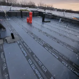 Montaż papy termozgrzewalnej BauderTEC KSA na płaskim dachu, widoczne butle z gazem Progas i elementy wentylacyjne