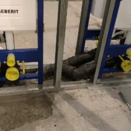 Dwa stelaże podtynkowe Geberit zamontowane w łazience w trakcie prac instalacyjnych, widoczne rury kanalizacyjne i elementy mocujące.