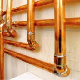 Miedziane rury instalacji centralnego ogrzewania, z widocznymi lutowanymi połączeniami, zamontowane przy ścianie.