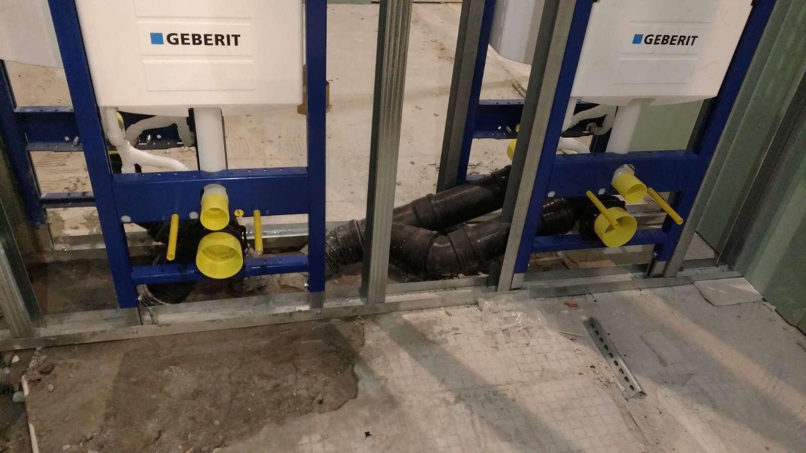 Dwa stelaże podtynkowe Geberit zamontowane w łazience w trakcie prac instalacyjnych, widoczne rury kanalizacyjne i elementy mocujące.