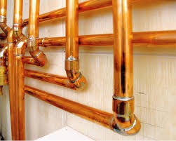 Miedziane rury instalacji centralnego ogrzewania, z widocznymi lutowanymi połączeniami, zamontowane przy ścianie.