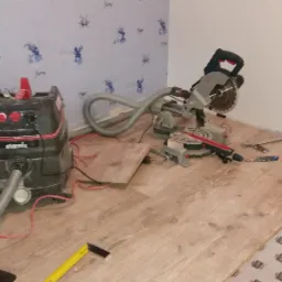 Układanie paneli podłogowych w Otwocku: widoczny odkurzacz przemysłowy Starmix, ukośnica Bosch, fragment ułożonych paneli oraz podkład pod panele z nadrukiem.