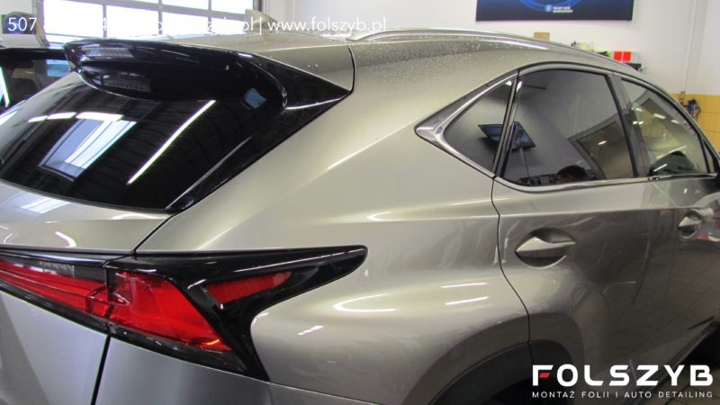 Szaro-beżowy Lexus NX z przyciemnionymi tylnymi szybami, widoczne logo firmy montującej folie na dolnej krawędzi zdjęcia.