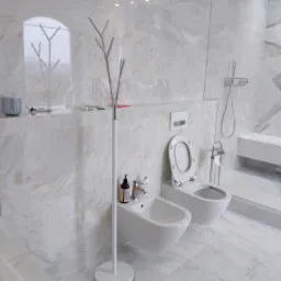 Jasna łazienka wykończona marmurowymi płytkami, z wiszącą toaletą, bidetem, minimalistycznym wieszakiem na ręczniki w kształcie drzewka oraz kabiną prysznicową w tle.