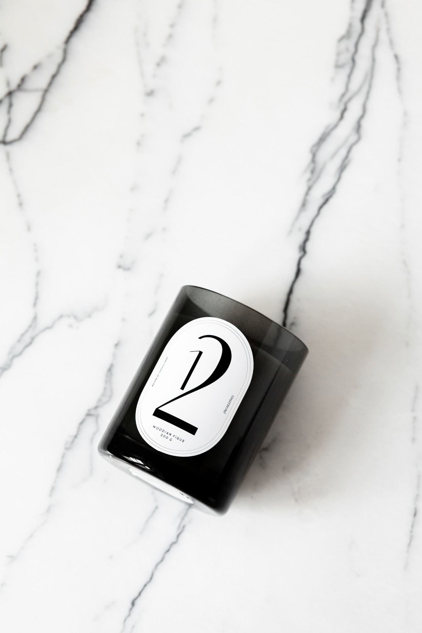 Ciemna szklana świeca zapachowa z białą etykietą z numerem '2' na marmurowym tle.