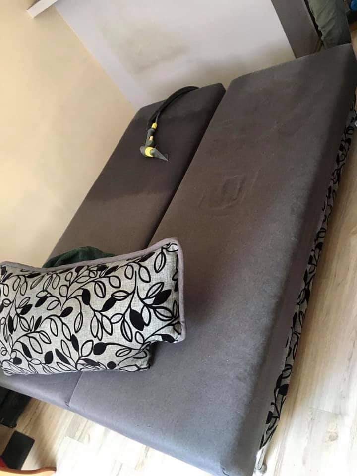 Szara sofa z poduszką w czarno-białe liście, na której leży dysza odkurzacza piorącego, widoczne ślady wilgoci po czyszczeniu.