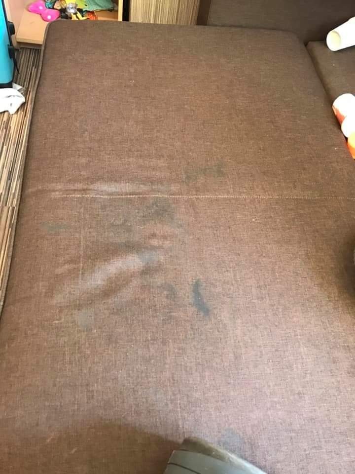 Brązowa tapicerka sofy z widocznymi plamami przed czyszczeniem, fragment odkurzacza widoczny w rogu