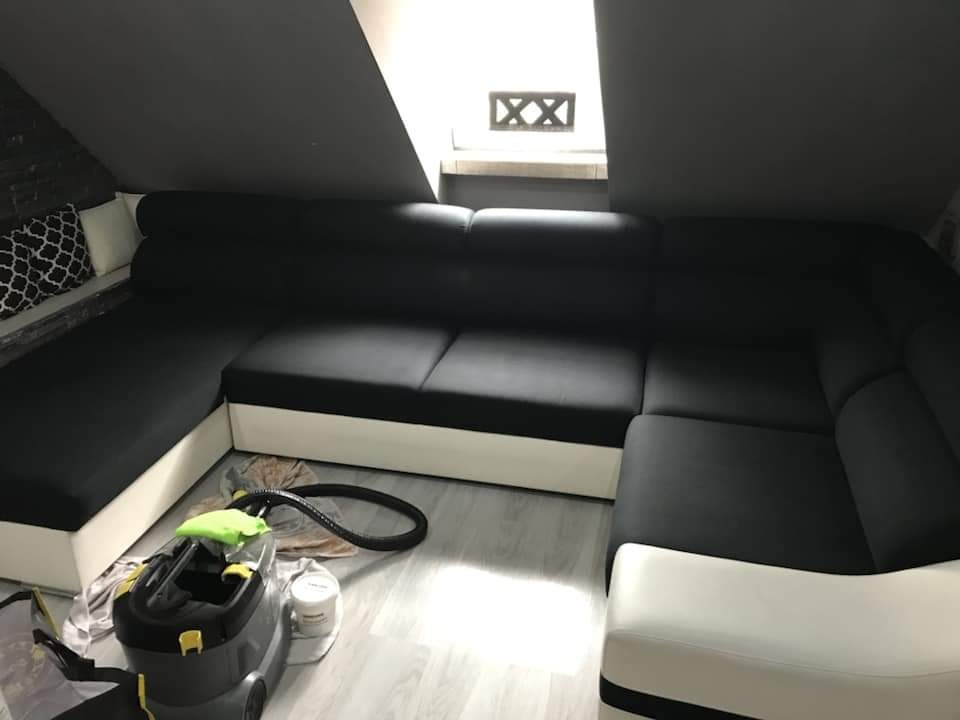 Czarno-biały narożnik w skosach poddasza, obok odkurzacz piorący z zieloną ściereczką, widoczny etap czyszczenia tapicerki.