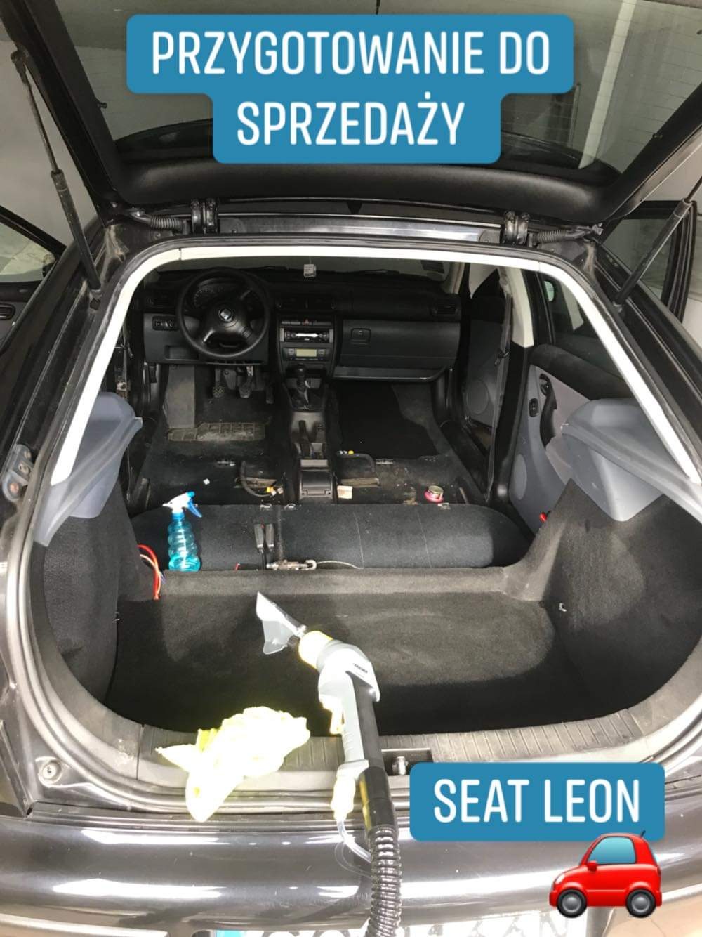 Wnętrze czarnego samochodu Seat Leon podczas prania tapicerki, widoczny od tyłu z otwartą klapą bagażnika, z użyciem odkurzacza piorącego i środka czyszczącego w sprayu.