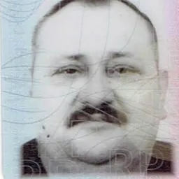 Czarno-białe zdjęcie portretowe mężczyzny z wąsami, z widocznymi śladami zarysowań i uszkodzeń na powierzchni zdjęcia.