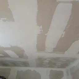 Niedokończone łączenia płyt gipsowo-kartonowych na suficie, widoczne pasy świeżo nałożonej masy szpachlowej, przygotowanie do dalszych prac wykończeniowych.