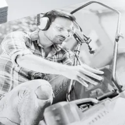 Mężczyzna w okularach ochronnych i słuchawkach naprawia kosiarkę na zdjęciu umieszczonym na wizytówce, obok stos wizytówek.