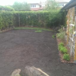 Maciej Żychowski - Przygotowany teren pod trawnik z rolki, widoczne fragmenty rozłożonej darni, obrzeża z kory i kamieni, oraz konstrukcja do pnących roślin przy ścianie budynku.