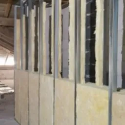 Montaż ścianki działowej z płyt gipsowo-kartonowych na poddaszu, widoczne metalowe profile, izolacja z wełny mineralnej oraz fragment drabiny.