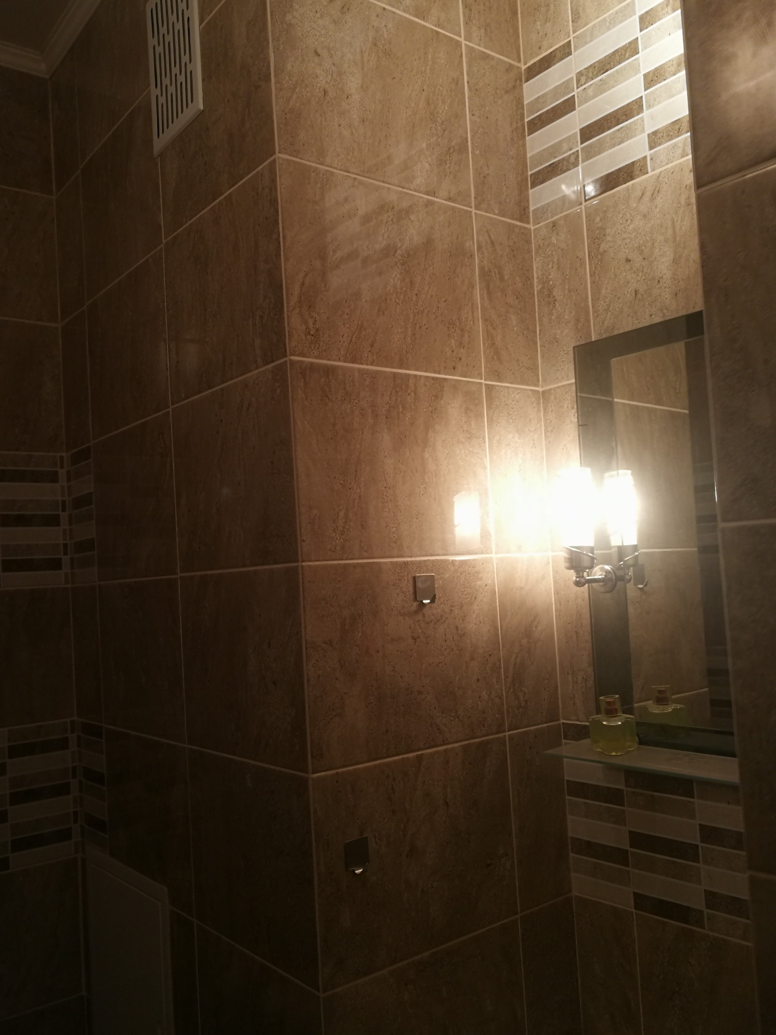 Wykończona łazienka w Wiskitkach z brązowymi płytkami imitującymi kamień, dekoracyjnym pasem z mozaiki, lustrem i oświetleniem nad umywalką.