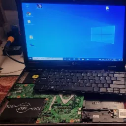 Otwarty laptop Dell z widoczną płytą główną i dyskiem SSD ASL, ekran z uruchomionym systemem Windows. Widoczne narzędzie serwisowe obok.