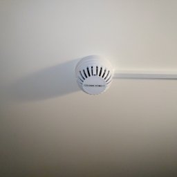 ELEKTRONET MARCIN BEREŚNIEWICZ - Biały czujnik dymu, model CZUJNIK DYMU-1, zamontowany na białym suficie, widoczna listwa przysufitowa.