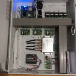 Panel sterowania alarmem z widocznymi modułami elektronicznymi, przewodami i diodami LED, zainstalowany w Gdańsku, wewnątrz białej obudowy.