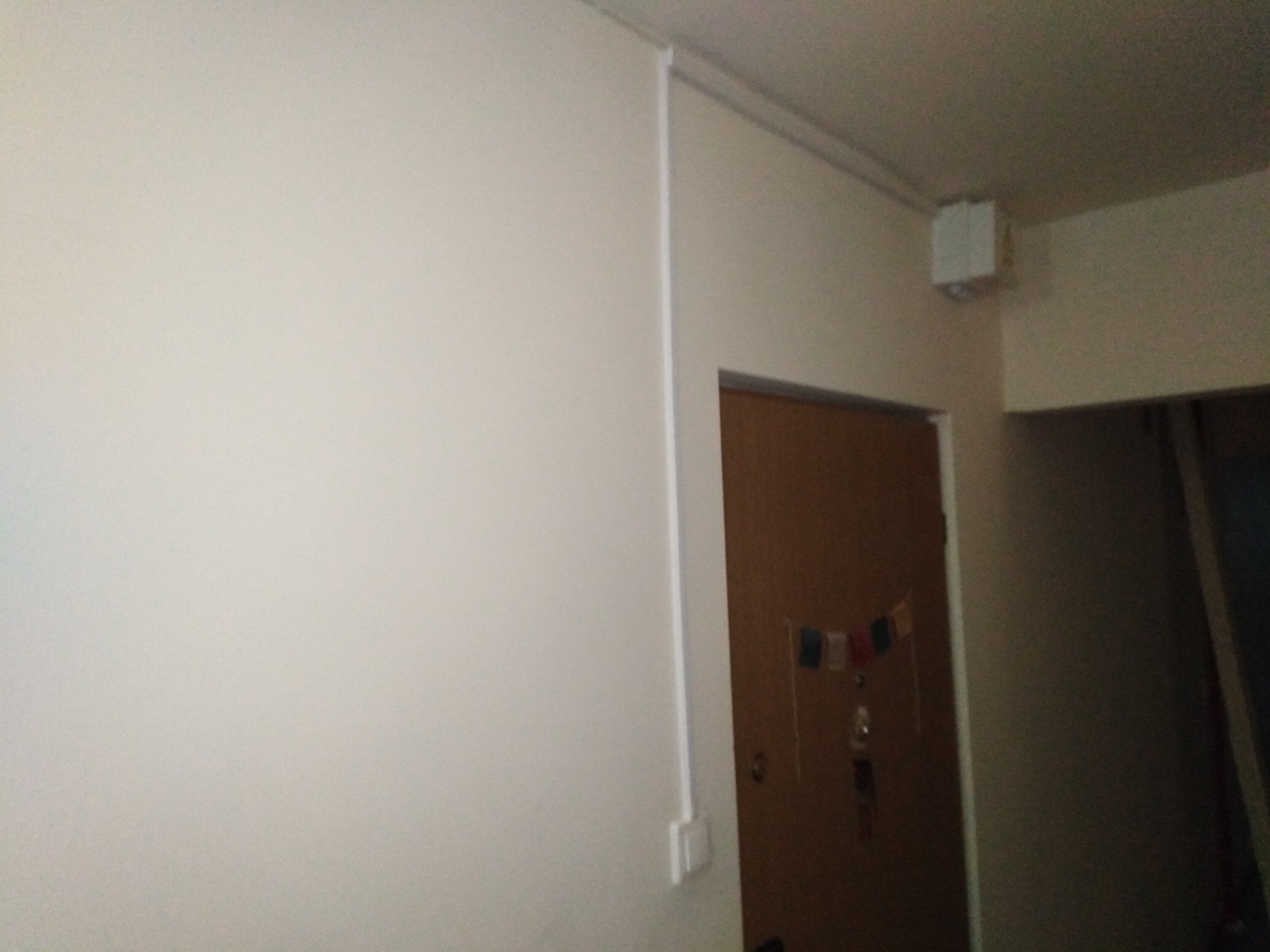 Fragment korytarza z widoczną instalacją elektryczną w białej listwie przypodłogowej, prowadzącą do domofonu przy drzwiach wejściowych, z zamontowanym elektrozaczepem sterowanym pilotem.