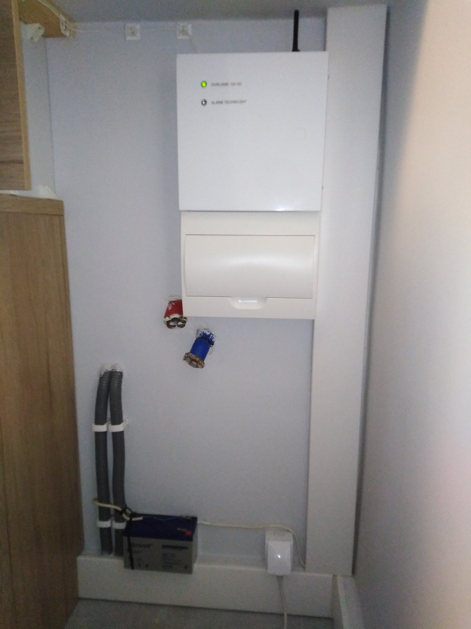 Centrala sterująca systemu detekcji alarmów technicznych z detekcją zalania i ulatniania gazu, z powiadamianiem GSM. Widoczne kable i akumulator.