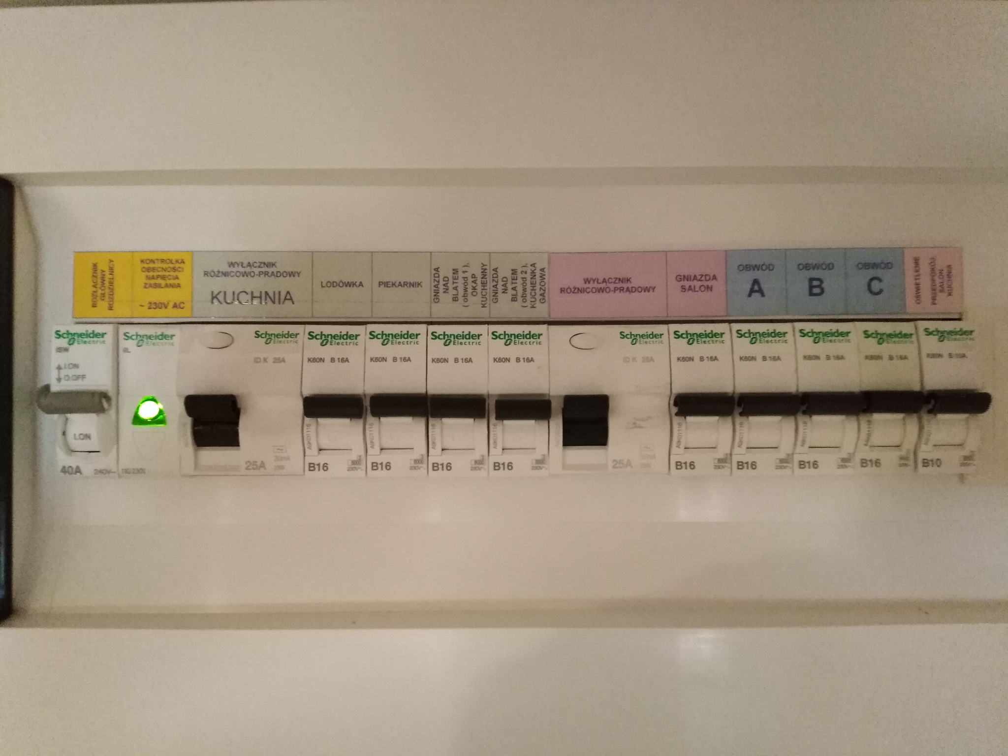 Rozdzielnica elektryczna Schneider z opisami obwodów (kuchnia, salon, lodówka, piekarnik) i włącznikami. Widoczna dioda sygnalizacyjna.