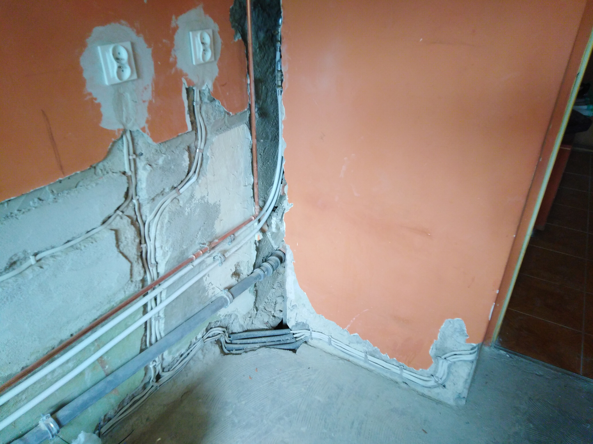 Fragment ściany z widocznymi przewodami elektrycznymi i gniazdkami w trakcie montażu. Widoczne rury i kable w ścianie, surowy stan wykończenia.
