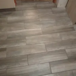 Ułożone podłużne płytki gresowe imitujące drewno, widoczne przy drzwiach i ścianie.