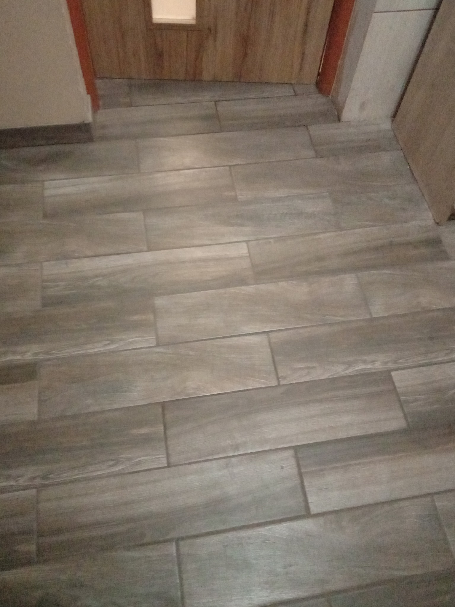 Ułożone podłużne płytki gresowe imitujące drewno, widoczne przy drzwiach i ścianie.