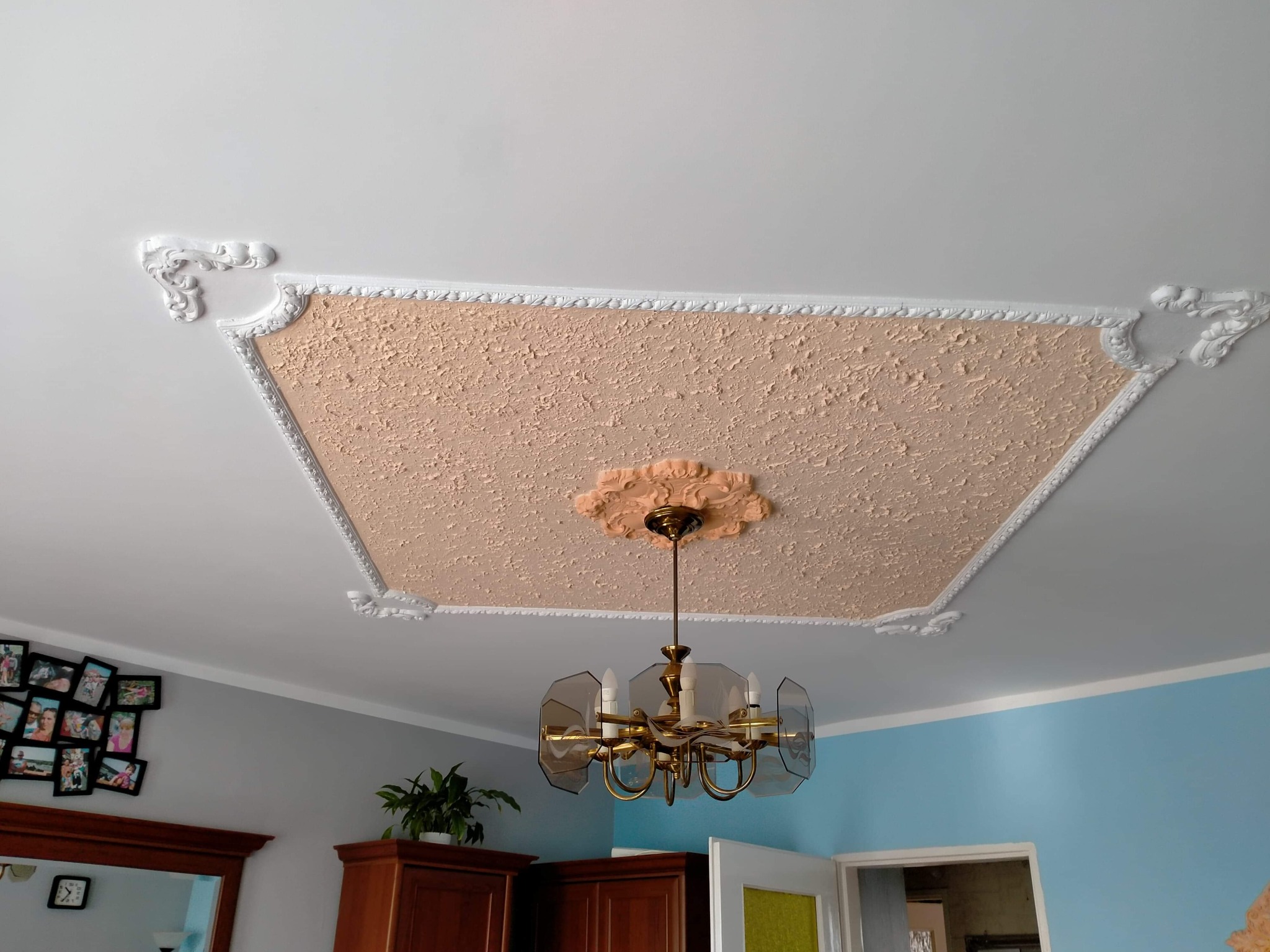 Dekoracyjny sufit z fakturą i sztukaterią, klasyczny żyrandol z przydymionymi kloszami.