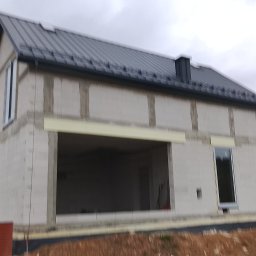 Usługi ogólnobudowlane - Surowy budynek z szarej cegły z zamontowanymi oknami i dachem z blachy trapezowej, widoczne elementy ocieplenia. Stan surowy otwarty.