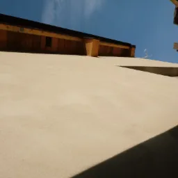 Jasna elewacja budynku widziana z dołu, fragment dachu i niebo w tle.