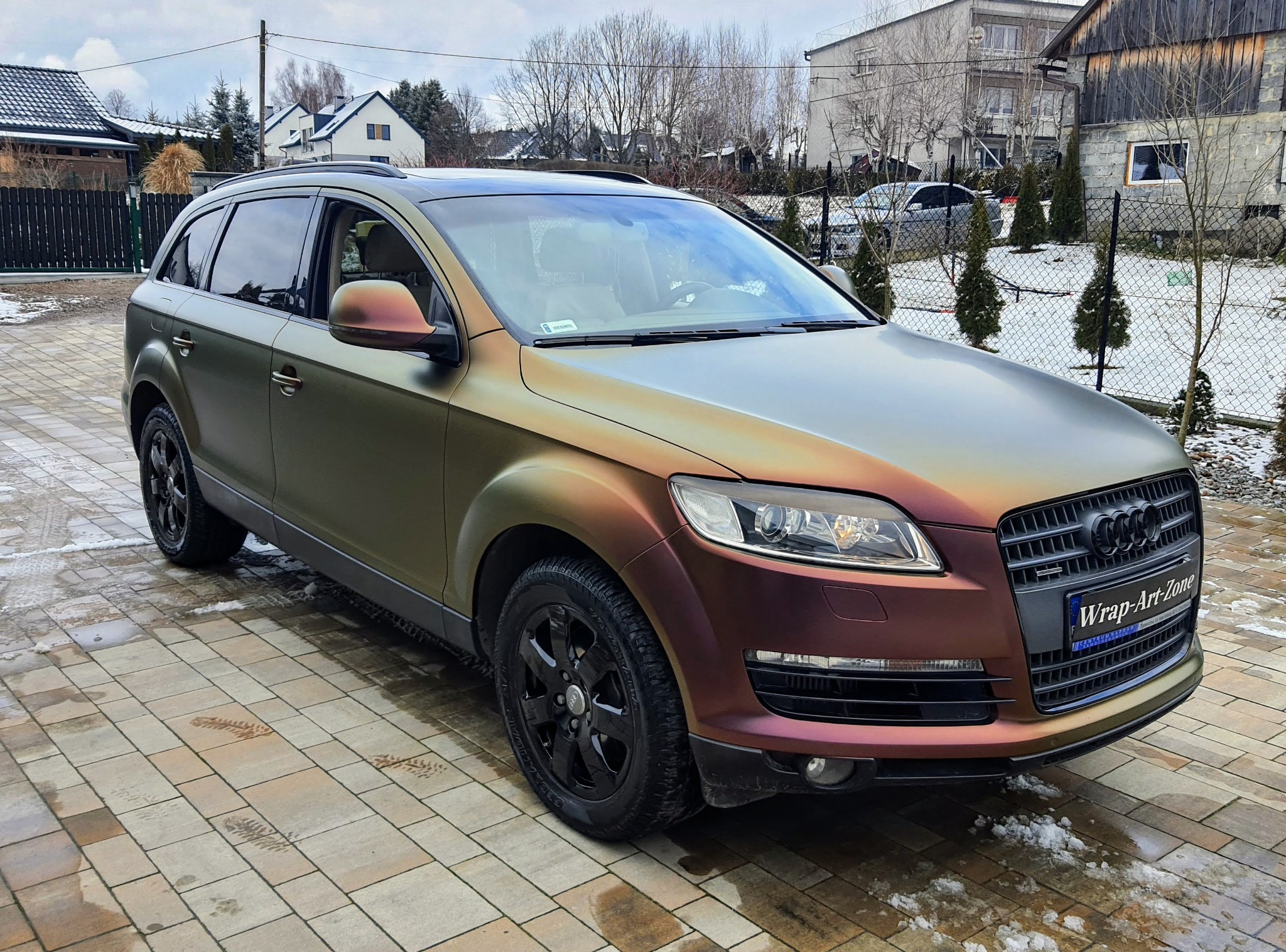 Audi Q7 z folią zmieniającą kolor od oliwkowego do miedzianego, zaparkowane na kostce brukowej w zimowej scenerii.