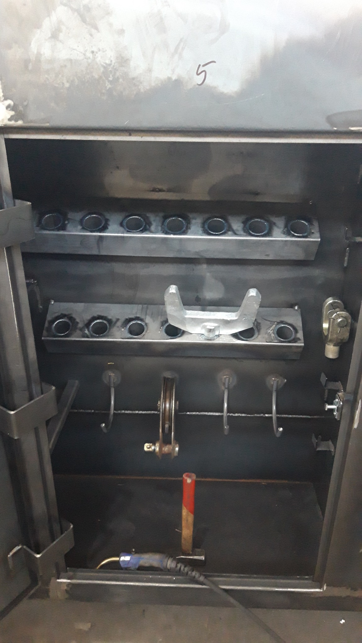 Wnętrze metalowej szafki warsztatowej z uchwytami na narzędzia, widoczne ślady spawania i użycia.