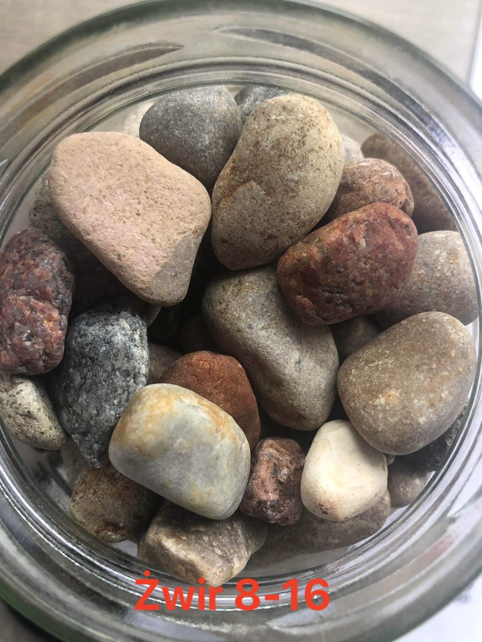 Różnokolorowe otoczaki w szklanym słoju, widoczne drobne ziarna i nierówności powierzchni.