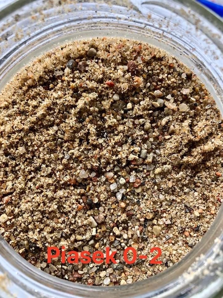 Bliski plan drobnego, brązowo-szarego kruszywa w szklanym słoiku z widocznymi różnymi frakcjami ziaren.