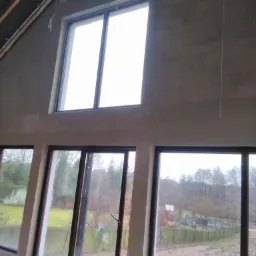 Surowe, szare ściany po nałożeniu tynku w nowo wybudowanym domu z dużymi oknami z widokiem na zewnątrz.